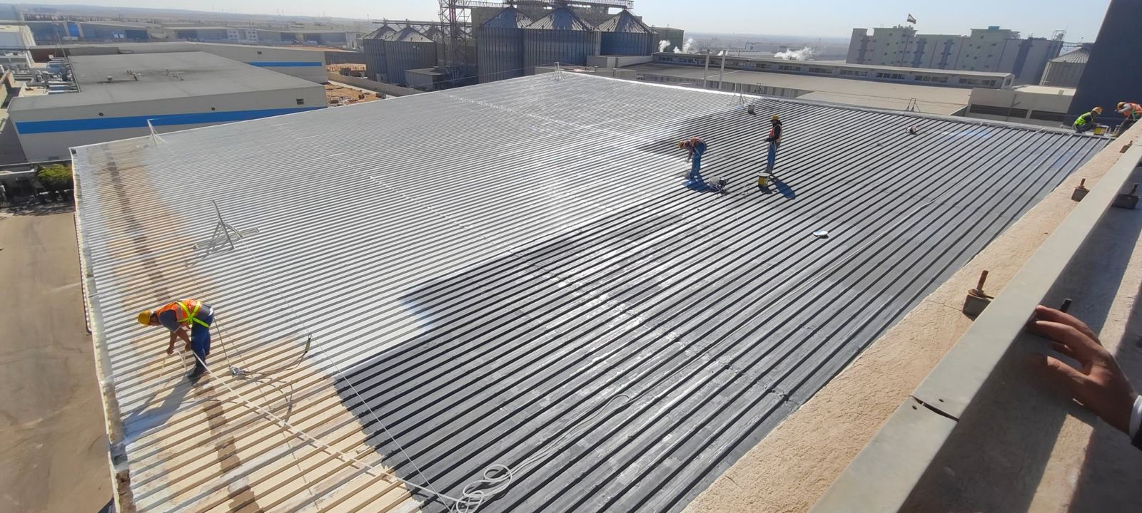 فنيون يطبقون طبقة عزل على سطح صاج معرّج لمصنع